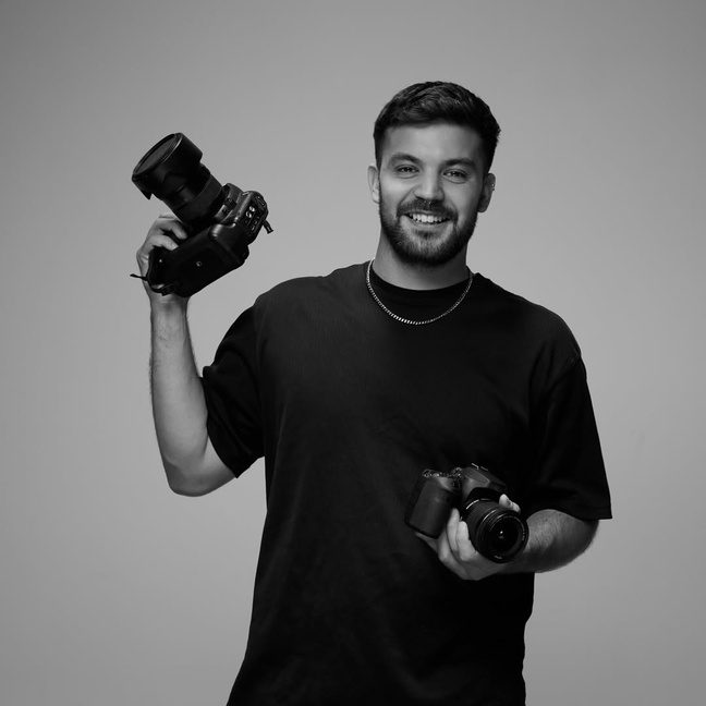 Portrait of Juani holding two cameras, in black and white
