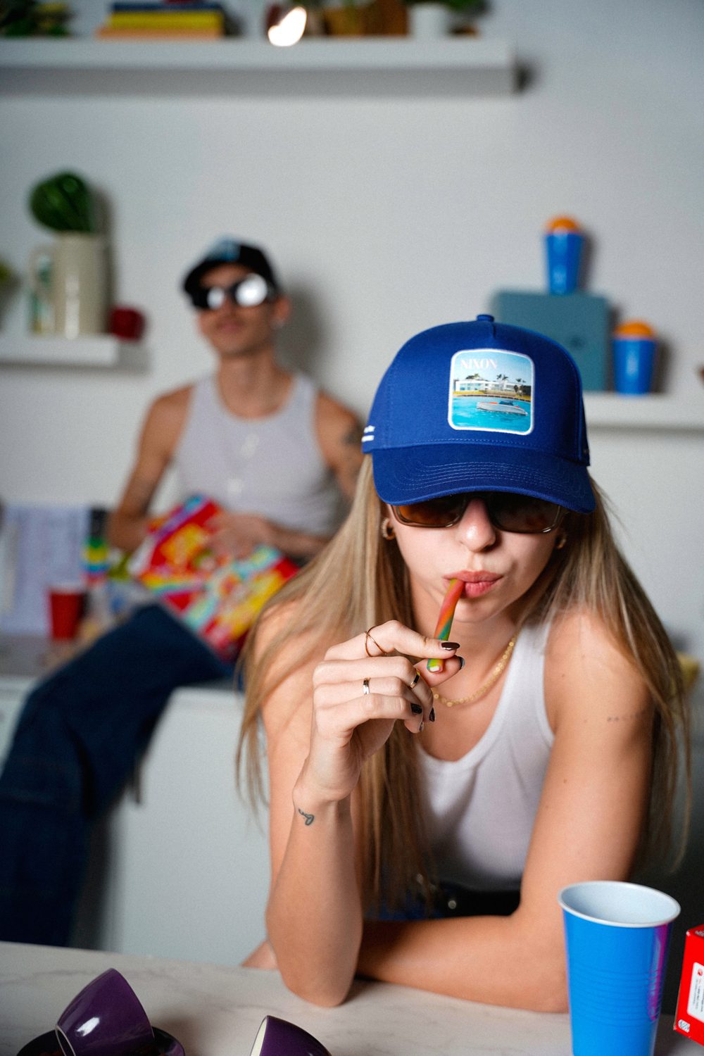 Woman in a blue trucker hat and sunglasses leaning on a kitchen counter